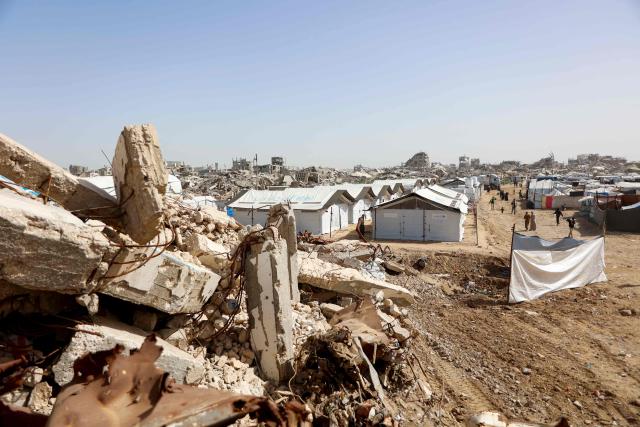 Palestinians walk next to shelters amid the rubble of destroyed buildings in Gaza City, on February 16, 2026. A US-brokered ceasefire, which sought to halt the fighting between Israel and Hamas sparked by the group's October 2023 attack, took effect last October, reducing the level of bombing and fighting in the Gaza Strip. (Photo by Omar AL-QATTAA / AFP)