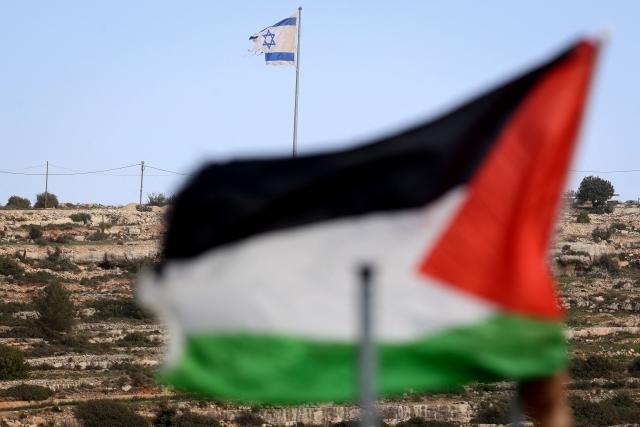 This picture taken from Umm Safa village, north of Ramallah in the occupied West Bank, shows a Palestinian flag (foreground) and Israeli flag fluttering on a hilltop overlooking the village on February 16, 2026. Israel's government has approved a process to register land in the West Bank as "state property", drawing condemnation from Arab nations and critics who said it would accelerate annexation of the Palestinian territory. (Photo by Zain JAAFAR / AFP)