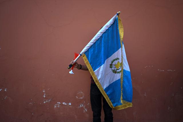 A demonstrator holds a national flag outside a hotel as University of San Carlos officials meet to appoint Constitutional Court magistrates, protesting the possible selection of Attorney General Consuelo Porras, in Antigua, Guatemala, on February 16, 2026. Guatemala has begun the process to renew members of key judicial institutions, including its top court and the Prosecutor's Office, which for years have been suspected of protecting a network of corruption and criminal activity. (Photo by JOHAN ORDONEZ / AFP)