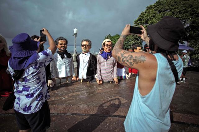 Revellers take snapshots of puppets depicting Brazilian actor Wagner Moura (L) and Brazilian film director Kleber Mendonca Filho (C) before the start of the Giant Puppets parade during carnival celebrations in the city of Olinda, Pernambuco state, Brazil, on February 16, 2026. This year, Brazilian film “O Agente Secreto” (The Secret Agent) was represented with giant puppets of director Kleber Mendonca Filho and actor Wagner Moura, along with the Pitombeiras street carnival group, a street party depicted in the film. (Photo by Diego Nigro / AFP)