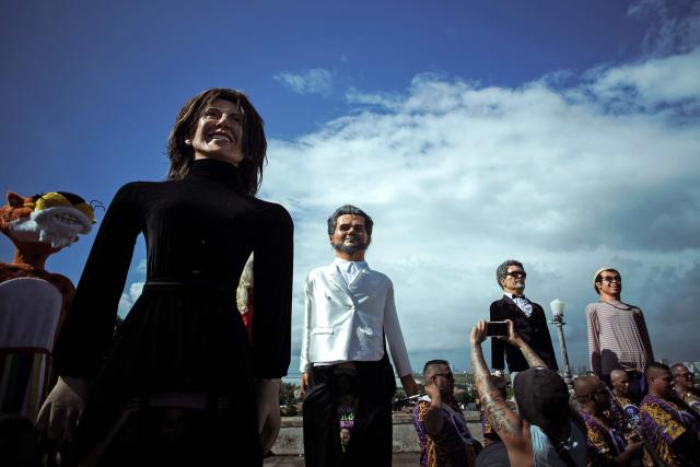 A reveller takes snapshots of puppets depicting Brazilian actress Fernanda Torres, actor Wagner Moura, and Brazilian film director Kleber Mendonca Filho (R) before the start of the Giant Puppets parade during carnival celebrations in the city of Olinda, Pernambuco state, Brazil, on February 16, 2026. This year, Brazilian film “O Agente Secreto” (The Secret Agent) was represented with giant puppets of director Kleber Mendonca Filho and actor Wagner Moura, along with the Pitombeiras street carnival group, a street party depicted in the film. (Photo by Diego Nigro / AFP)