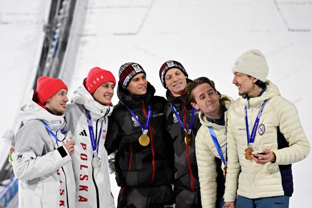(fromL) Silver medallists Poland's Kacper Tomasiak, Poland's Pawel Wasek, gold medallists Austria's Stephan Embacher, Austria's Jan Hoerl, bronze medallists Norway's Kristoffer Eriksen Sundal and Norway's Johann Andre Forfang celebrate on the podium for the men's large hill super team ski jumping of the Milano Cortina 2026 Winter Olympic Games at Predazzo Ski Jumping Stadium in Predazzo (Val di Fiemme), on February 16, 2026. (Photo by Tobias SCHWARZ / AFP)