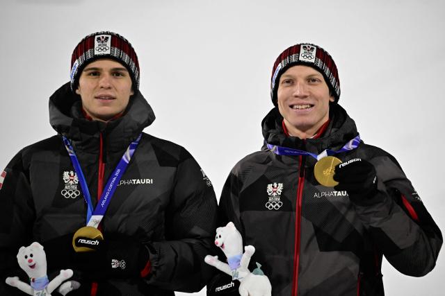 Gold medallists Austria's Stephan Embacher (L) and Austria's Jan Hoerl celebrate on the podium for the men's large hill super team ski jumping of the Milano Cortina 2026 Winter Olympic Games at Predazzo Ski Jumping Stadium in Predazzo (Val di Fiemme), on February 16, 2026. (Photo by Tobias SCHWARZ / AFP)