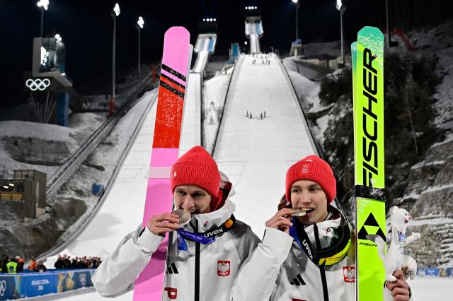 Silver medallists Poland's Kacper Tomasiak (R) and Poland's Pawel Wasek celebrate on the podium for the men's large hill super team ski jumping of the Milano Cortina 2026 Winter Olympic Games at Predazzo Ski Jumping Stadium in Predazzo (Val di Fiemme), on February 16, 2026. (Photo by Tobias SCHWARZ / AFP)
