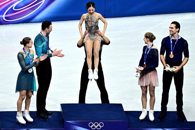 Silver medallists (L) Georgia's Anastasiia Metelkina and Luka Berulava, gold medallists (C) Japan's Riku Miura and Ryuichi Kihara and bronze medallists (R) Germany's Minerva Fabienne Hase and Nikita Volodin celebrate on the podium of the figure skating pair skating free skating final during the Milano Cortina 2026 Winter Olympic Games at Milano Ice Skating Arena in Milan on February 16, 2026. (Photo by JULIEN DE ROSA / AFP)