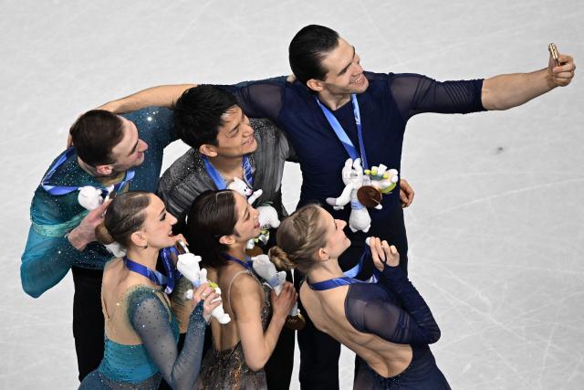 Silver medallists Georgia's Anastasiia Metelkina and Georgia's Luka Berulava, gold medallists Japan's Riku Miura and Japan's Ryuichi Kihara, and bronze medallists Germany's Minerva Fabienne Hase and Germany's Nikita Volodin pose for a selfie on the podium of the figure skating pair skating free skating final during the Milano Cortina 2026 Winter Olympic Games at Milano Ice Skating Arena in Milan on February 16, 2026. (Photo by Antonin THUILLIER / AFP)