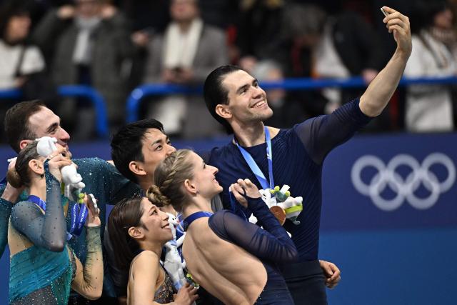 Silver medallists Georgia's Anastasiia Metelkina and Georgia's Luka Berulava, gold medallists Japan's Riku Miura and Japan's Ryuichi Kihara, and bronze medallists Germany's Minerva Fabienne Hase and Germany's Nikita Volodin pose for a selfie on the podium of the figure skating pair skating free skating final during the Milano Cortina 2026 Winter Olympic Games at Milano Ice Skating Arena in Milan on February 16, 2026. (Photo by Gabriel BOUYS / AFP)