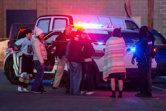 People embrace and walk away as police stand outside the perimeter they created around the Dennis M. Lynch Arena where a shooting occurred earlier today in Pawtucket, Rhode Island, on February 16, 2026. At least two people were killed and three wounded in a shooting at an ice rink in the northeastern US town of Pawtucket on Monday, authorities said, with social media footage showing frightened teenagers fleeing the sound of gunshots. "We have three deceased. The suspect, and then we have two victims, and then we have three at the hospital," said Pawtucket police chief Tina Goncalves told reporters after the incident. She added that initial investigations suggested the shooting was targeted and "may be a family dispute." (Photo by Joseph Prezioso / AFP)