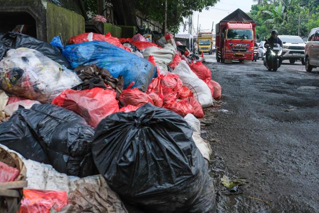 This picture taken on January 20, 2026, shows vehicles driving along a road littered with illegally dumped waste by residents in Pamulang, South Tangerang, Banten. Garbage-choked streets, overloaded landfills and the fear of trash avalanches haunt greater Jakarta, as the world's most populous metropolis grapples with a waste crisis. (Photo by BAY ISMOYO / AFP) / To go with 'INDONESIA-ENVIRONMENT-WASTE-CRISIS,FOCUS' by Dessy SAGITA