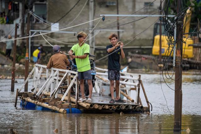 This picture taken on January 15, 2026, shows residents passing by electrical installations while using a boat to cross a public road that has been submerged for years by rising river levels following trash avalanches at the Cipayung landfill, Depok, West Java. Garbage-choked streets, overloaded landfills and the fear of trash avalanches haunt greater Jakarta, as the world's most populous metropolis grapples with a waste crisis. (Photo by BAY ISMOYO / AFP) / To go with 'INDONESIA-ENVIRONMENT-WASTE-CRISIS,FOCUS' by Dessy SAGITA