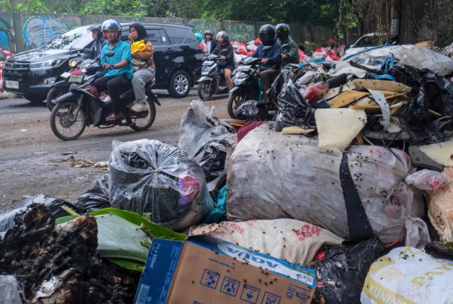 This picture taken on January 20, 2026, shows vehicles driving along a road littered with illegally dumped waste by residents in Pamulang, South Tangerang, Banten. Garbage-choked streets, overloaded landfills and the fear of trash avalanches haunt greater Jakarta, as the world's most populous metropolis grapples with a waste crisis. (Photo by BAY ISMOYO / AFP) / To go with 'INDONESIA-ENVIRONMENT-WASTE-CRISIS,FOCUS' by Dessy SAGITA