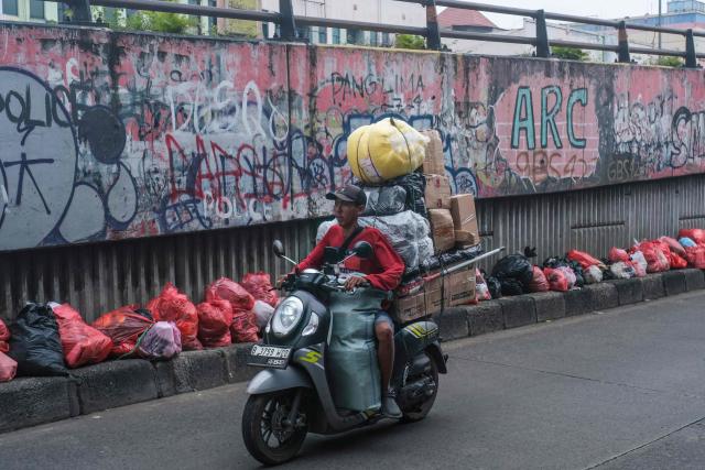 This picture taken on January 20, 2026, shows a motorcyclist riding along a road littered with illegally dumped waste by residents in Ciputat, South Tangerang, Banten. Garbage-choked streets, overloaded landfills and the fear of trash avalanches haunt greater Jakarta, as the world's most populous metropolis grapples with a waste crisis. (Photo by BAY ISMOYO / AFP) / To go with 'INDONESIA-ENVIRONMENT-WASTE-CRISIS,FOCUS' by Dessy SAGITA