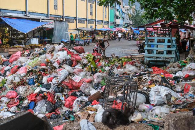 This picture taken on January 20, 2026, shows a man (C) tidying a pile of garbage on a public road in Pasar Minggu, Jakarta. Garbage-choked streets, overloaded landfills and the fear of trash avalanches haunt greater Jakarta, as the world's most populous metropolis grapples with a waste crisis. (Photo by BAY ISMOYO / AFP) / To go with 'INDONESIA-ENVIRONMENT-WASTE-CRISIS,FOCUS' by Dessy SAGITA
