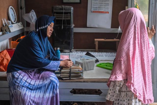 This picture taken on February 4, 2026, shows a staff member of a waste bank that purchases recylable material brought in by the community, receiving paper waste from a local resident in Jakarta. Garbage-choked streets, overloaded landfills and the fear of trash avalanches haunt greater Jakarta, as the world's most populous metropolis grapples with a waste crisis. (Photo by BAY ISMOYO / AFP) / To go with 'INDONESIA-ENVIRONMENT-WASTE-CRISIS,FOCUS' by Dessy SAGITA