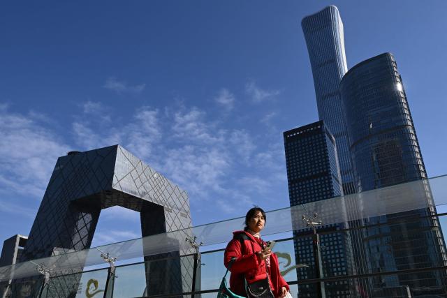 This picture taken on February 11, 2026 shows a pedestrian walking past the China Central Television (CCTV) headquarters in the background on a clear day in Beijing. Fifteen years ago, Beijing's Liangma riverbanks would have been smog-choked and deserted in winter, but these days they are dotted with families and exercising pensioners most mornings. The turnaround is the result of a years-long campaign that threw China's state power behind policies like moving factories and electrifying vehicles to improve some the world's worst air pollution. (Photo by Pedro PARDO / AFP) / To go with AFP story China-environment-air pollition-politics, FOCUS by Peter Catterall and Rebecca Bailey