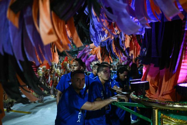 Float pushers of the Beija-Flor de Nipolis samba school gesture during the second night of the Rio Carnival at the Marques de Sapucai Sambadrome in Rio de Janeiro, Brazil, early on February 17, 2026. (Photo by Mauro PIMENTEL / AFP)