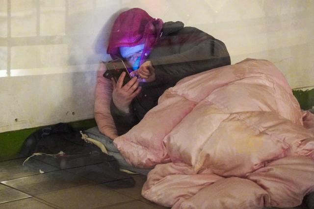 A woman looks at her phone as she takes shelter at a metro station during an air raid alert, in Kyiv, early on February 17, 2026, amid the Russian invasion of Ukraine. (Photo by Serhii Okunev / AFP)