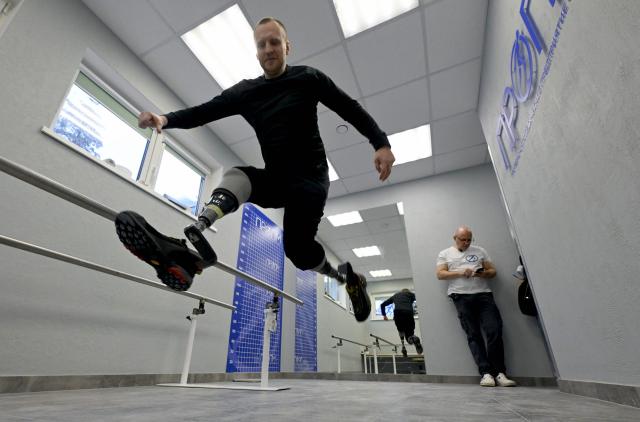 A patient runs on prosthetic limbs as Mikhail Moskovtsev, 53, the private prosthetics workshop head, uses his smartphone at the studio's grounds in the Leningrad region on January 22, 2026. (Photo by Olga MALTSEVA / AFP)
