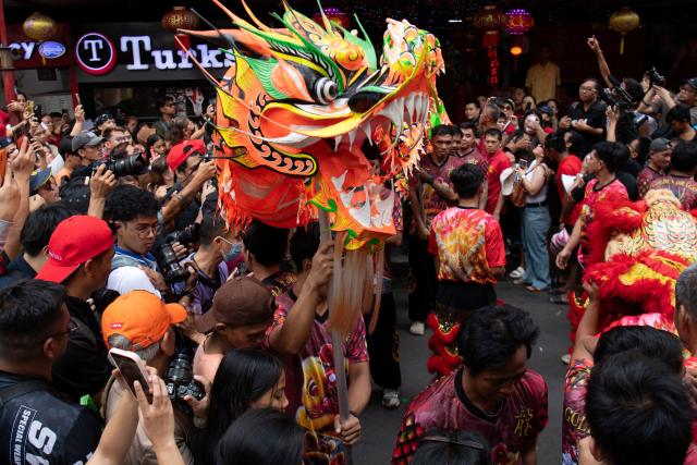 People watch a dragon dance group perform along a street during the first day of the Lunar New Year of the Horse in the Chinatown district of Manila on February 17, 2026. (Photo by Ted ALJIBE / AFP)