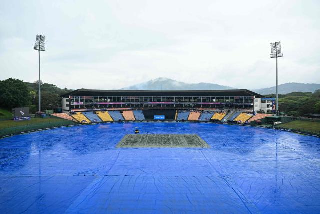 The ground remains covered in tarpaulin as rain delays the start of the 2026 ICC Men's T20 Cricket World Cup group stage match between Zimbabwe and Ireland at Pallekele International Cricket Stadium in Kandy on February 17, 2026. (Photo by Ishara S. KODIKARA / AFP)