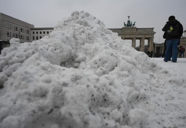 Tourists walk past ploughed snow in front of the Brandenburg Gate in Berlin, on February 17, 2026 after new snowfall. (Photo by RALF HIRSCHBERGER / AFP)
