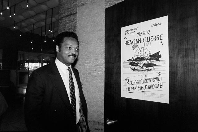 (FILES) Democratic presidential candidate Jesse Jackson passes on May 7, 1985 near a poster, reading "No to Reagan to war", against the incoming visit of US President Ronald Reagan at the European Parliament in Strasbourg. Veteran US civil rights activist Reverend Jesse Jackson died on February 17, 2026, his family said in a statement. He was 84. (Photo by Marcel MOCHET / AFP)