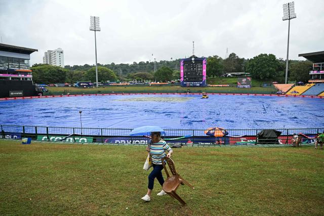 TOPSHOT - A cricket fan carrying an umbrella walks past the covered pitch as rain delays the start of the 2026 ICC Men's T20 Cricket World Cup group stage match between Zimbabwe and Ireland at Pallekele International Cricket Stadium in Kandy on February 17, 2026. (Photo by Ishara S. KODIKARA / AFP)