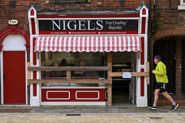 A man jogs past a shop which has been boarded up to protect its frontage, ahead of the annual Royal Shrovetide Football match in Ashbourne, northern England on February 17, 2026. The mass-participation ball game involves two teams, whose players are defined by which side of a small brook that bisects the town they were born, aiming to score a goal, which are some three miles (4.8 km) apart. The game, which has very few rules and believed to have been played annually since 1667, is played over two eight hour periods on Shrove Tuesday and Ash Wednesday. (Photo by Paul ELLIS / AFP)