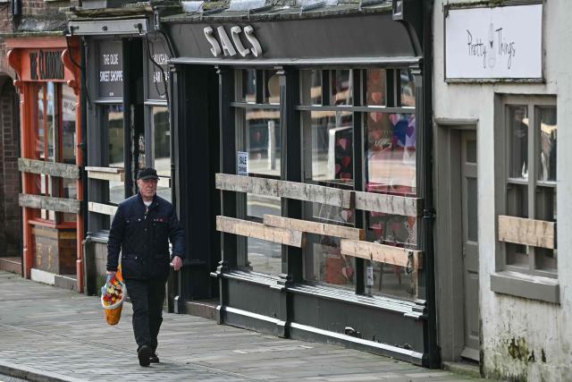 A pedestrian walks past a shop which has been boarded up to protect its frontage, ahead of the annual Royal Shrovetide Football match in Ashbourne, northern England on February 17, 2026. The mass-participation ball game involves two teams, whose players are defined by which side of a small brook that bisects the town they were born, aiming to score a goal, which are some three miles (4.8 km) apart. The game, which has very few rules and believed to have been played annually since 1667, is played over two eight hour periods on Shrove Tuesday and Ash Wednesday. (Photo by Paul ELLIS / AFP)