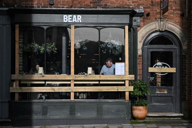 Customers sit in the window of a shop which has been boarded up to protect its frontage, ahead of the annual Royal Shrovetide Football match in Ashbourne, northern England on February 17, 2026. The mass-participation ball game involves two teams, whose players are defined by which side of a small brook that bisects the town they were born, aiming to score a goal, which are some three miles (4.8 km) apart. The game, which has very few rules and believed to have been played annually since 1667, is played over two eight hour periods on Shrove Tuesday and Ash Wednesday. (Photo by Paul ELLIS / AFP)