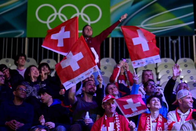 Supporters of Team Switzerland wave flags in the stands ahead of the men's qualification play-off ice hockey match between Switzerland and Italy during the Milano Cortina 2026 Winter Olympic Games at the Milano Rho Ice Hockey Arena in Milan, on February 17, 2026. (Photo by Piero CRUCIATTI / AFP)