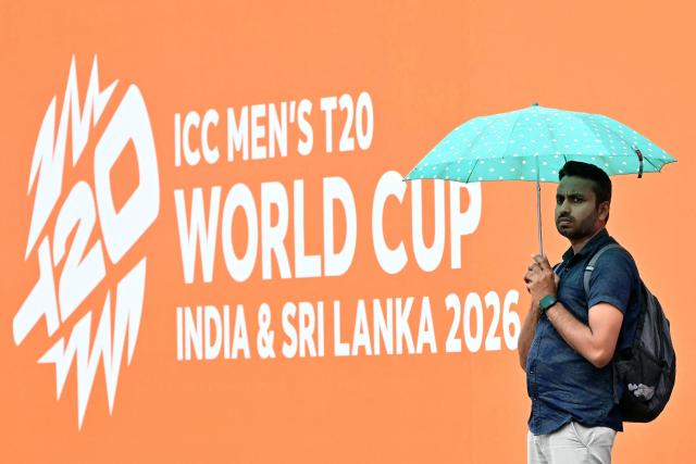 A cricket fan takes shelter under an umbrella as rain delays the start of the 2026 ICC Men's T20 Cricket World Cup group stage match between Zimbabwe and Ireland at Pallekele International Cricket Stadium in Kandy on February 17, 2026. (Photo by Ishara S. KODIKARA / AFP)