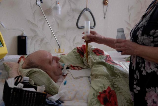 Olena Grygorenko feeds her husband Anatoli Kuchynsky in Chernihiv on February 12, 2026, amid the Russian invasion of Ukraine. Olena Grygorenko has barely left her Chernigiv flat in the past weeks. Every time a blackout hits the city, she rushes to her husband's bedside to plug his life support machine into its back-up batteries. Bedridden, completely paralysed and connected 24/7 to a life support machine, her husband Anatoli Kuchynsky suffers amyotrophic lateral sclerosis (ALS) - an incurable degenerative nerve disease. Russia's incessant strikes on Ukraine's energy grid over the last month have made their fight against the condition even more perilous. (Photo by Tetiana DZHAFAROVA / AFP)