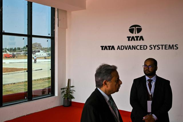 Men stand next to a sign of Tata Advanced Systems ahead of the virtual inauguration of the H125 Light Utility Helicopter's Final Assembly Line (FAL) facility of Tata-Airbus at Vemagal on February 17, 2026. Indian Prime Minister Narendra Modi and French President Emmanuel Macron will inaugurate, via video conference on February 17, India's first helicopter final assembly line, a joint venture between India's Tata Group and Airbus. (Photo by Idrees MOHAMMED / AFP)
