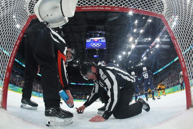 Referees inspect the ice under France's goalpost during the men's qualification play-off ice hockey match between Germany and France at the Milano Santagiulia Ice Hockey Arena during the Milano Cortina 2026 Winter Olympic Games in Milan, on February 17, 2026. (Photo by POOL / AFP)