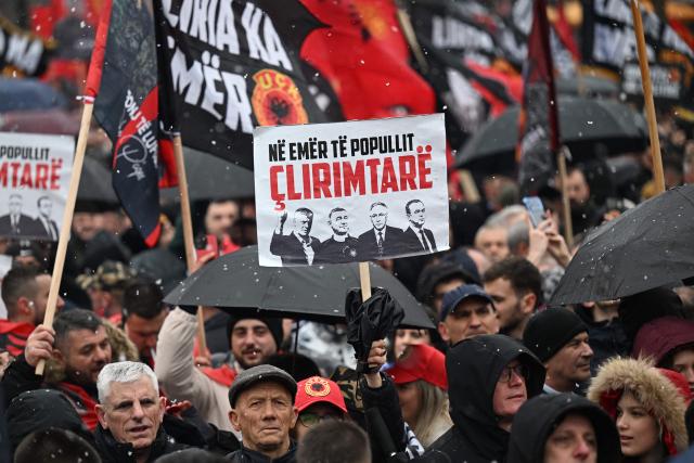 A protestor holds a placard displaying the faces of former Kosovo Liberation Army (KLA) leaders including former Kosovo President Hashim Thaci during a demonstration in downtown Pristina in support of former KLA leaders on trial at the international tribunal in The Hague on February 17, 2026. (Photo by Armend NIMANI / AFP)