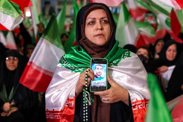 A woman holds a phone displaying a picture of a slain person during a memorial ceremony marking the 40th day of mourning for victims of "terrorism" killed in previous anti-government protests in Iran, at the Tehran Musalla on February 17, 2026. (Photo by ATTA KENARE / AFP)