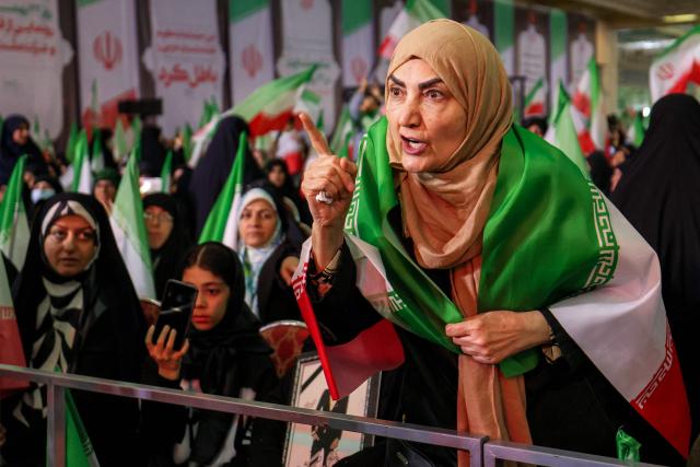 TOPSHOT - A woman draped in the Iranian flag speaks before the government spokesperson (outside frame) attending a memorial ceremony marking the 40th day of mourning for victims of "terrorism" killed in previous anti-government protests in Iran, at the Tehran Musalla on February 17, 2026. (Photo by ATTA KENARE / AFP)