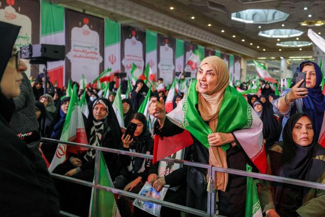 TOPSHOT - A woman draped in the Iranian flag speaks before the government spokesperson Fatemeh Mohajerani (L) attending a memorial ceremony marking the 40th day of mourning for victims of "terrorism" killed in previous anti-government protests in Iran, at the Tehran Musalla on February 17, 2026. (Photo by ATTA KENARE / AFP)