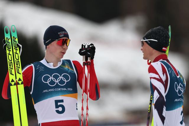 Norway's Jens Luraas Oftebro (L) talks with a fellow athlete after crossing the finish to win overall gold, in the cross-country event of the nordic combined individual Gundersen large hill/10km at Tesero Cross Country Stadium at Lago di Tesero (Val di Fiemme) during the Milano Cortina 2026 Winter Olympic Games on February 17, 2026. (Photo by Anne-Christine POUJOULAT / AFP)