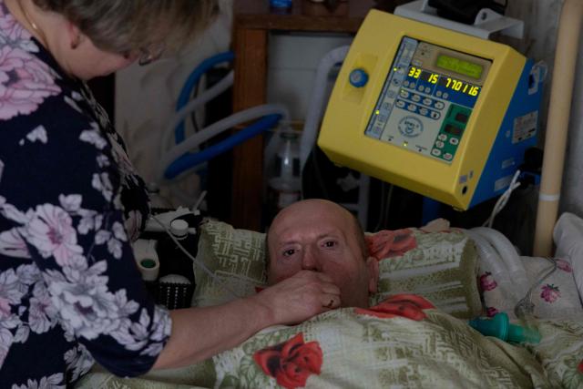 Olena Grygorenko feeds her husband Anatoli Kuchynsky in Chernihiv on February 12, 2026, amid the Russian invasion of Ukraine. Olena Grygorenko has barely left her Chernigiv flat in the past weeks. Every time a blackout hits the city, she rushes to her husband's bedside to plug his life support machine into its back-up batteries. Bedridden, completely paralysed and connected 24/7 to a life support machine, her husband Anatoli Kuchynsky suffers amyotrophic lateral sclerosis (ALS) - an incurable degenerative nerve disease. Russia's incessant strikes on Ukraine's energy grid over the last month have made their fight against the condition even more perilous. (Photo by Tetiana DZHAFAROVA / AFP)