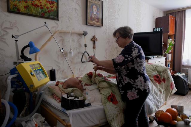 Olena Grygorenko feeds her husband Anatoli Kuchynsky in Chernihiv on February 12, 2026, amid the Russian invasion of Ukraine. Olena Grygorenko has barely left her Chernigiv flat in the past weeks. Every time a blackout hits the city, she rushes to her husband's bedside to plug his life support machine into its back-up batteries. Bedridden, completely paralysed and connected 24/7 to a life support machine, her husband Anatoli Kuchynsky suffers amyotrophic lateral sclerosis (ALS) - an incurable degenerative nerve disease. Russia's incessant strikes on Ukraine's energy grid over the last month have made their fight against the condition even more perilous. (Photo by Tetiana DZHAFAROVA / AFP)