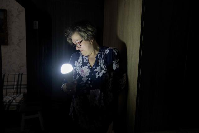 Olena Grygorenko holds a lamp in her hands during a power outage in Chernihiv on February 12, 2026, amid the Russian invasion of Ukraine. Olena Grygorenko has barely left her Chernigiv flat in the past weeks. Every time a blackout hits the city, she rushes to her husband's bedside to plug his life support machine into its back-up batteries. Bedridden, completely paralysed and connected 24/7 to a life support machine, her husband Anatoli Kuchynsky suffers amyotrophic lateral sclerosis (ALS) - an incurable degenerative nerve disease. Russia's incessant strikes on Ukraine's energy grid over the last month have made their fight against the condition even more perilous. (Photo by Tetiana DZHAFAROVA / AFP)
