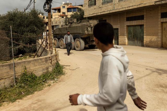 Palestinian men walk past an Israeli armored vehicle during a military raid in al-Yamun town west of Jenin in the occupied West Bank on February 17, 2026. (Photo by JOHN WESSELS / AFP)
