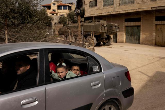 TOPSHOT - A Palestinian family look out the window as they drive past an Israeli armored vehicle during a military raid in al-Yamun town west of Jenin in the occupied West Bank on February 17, 2026. (Photo by JOHN WESSELS / AFP)