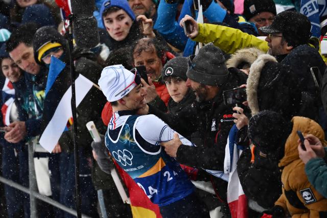 France's Eric Perrot (L) celebrates with relatives after winning the men's biathlon 4 x 7,5km relay event during the Milano Cortina 2026 Winter Olympic Games at the Anterselva Biathlon Arena (Sudtirol Arena) in Anterselva (Val Pusteria) on February 17, 2026. (Photo by Marco BERTORELLO / AFP)