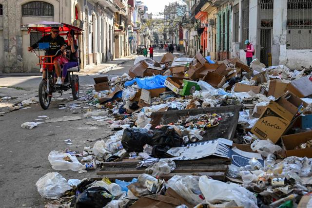 A bicitaxi rides past garbage piled up on a street in Havana on February 17, 2026. (Photo by YAMIL LAGE / AFP)