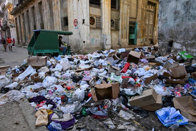 An electric tricycle drives past garbage piled up on a street in Havana on February 17, 2026. (Photo by YAMIL LAGE / AFP)