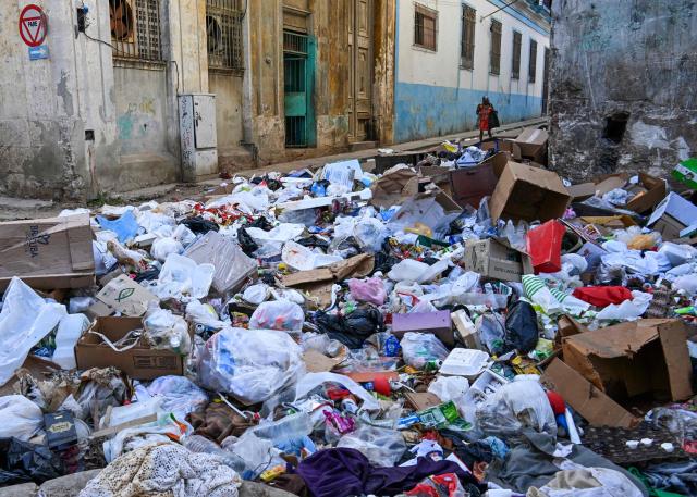 A woman walks by garbage piled up on a street in Havana on February 17, 2026. (Photo by YAMIL LAGE / AFP)