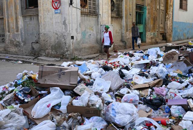 People walk past garbage piled up on a street in Havana on February 17, 2026. (Photo by YAMIL LAGE / AFP)